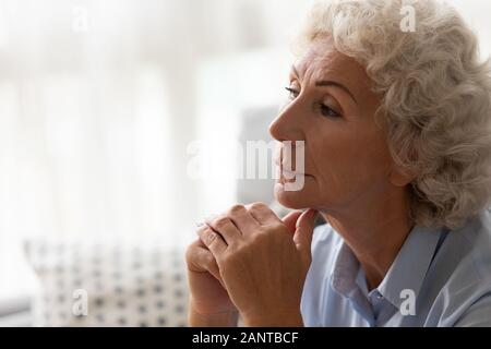 Close up thoughtful older woman worried about problem, sitting alone Stock Photo