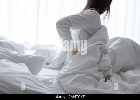 Woman sitting in bed, massaging back, feeling pain after awakening Stock Photo