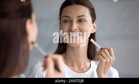 Smiling beautiful woman looking in mirror, holding makeup brush Stock Photo