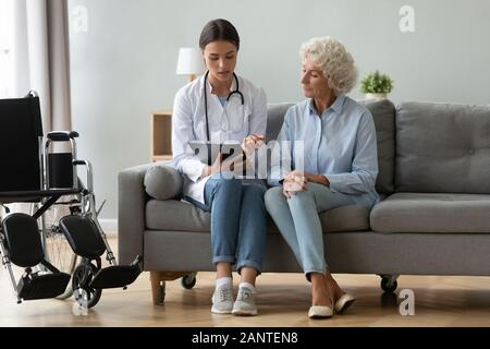 Doctor consulting disabled older woman, filling patient medical form Stock Photo