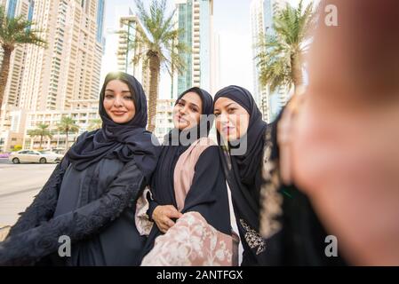 Arabic women with abaya bonding and having fun outdoors - Happy middleastern friends meeting and talking while shopping Stock Photo