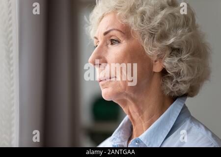 Close up thoughtful older woman looking out window at home Stock Photo