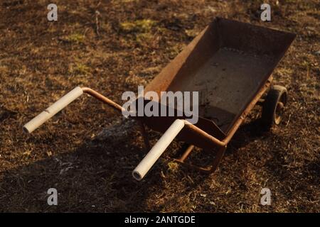 Old rusty trolley on wheels standing on the ground with dry grass. Stock Photo