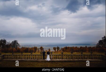 bride and groom under an black umbrellas in the rainy weather near the castle. photo from afar. Stock Photo