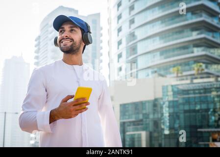 Middle-eastern young adult wearing kandora walking outdoors in Dubai - Arabic man wearing the traditional emirates clothes Stock Photo