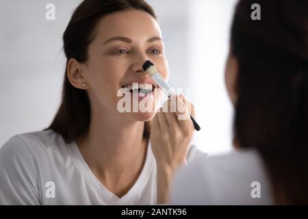 Smiling woman looking in mirror, applying makeup with brush Stock Photo
