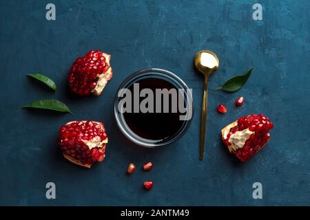 Pomegranate sauce in a transparent bowl and slices of pomegranate on a dark blue background. View from above Stock Photo