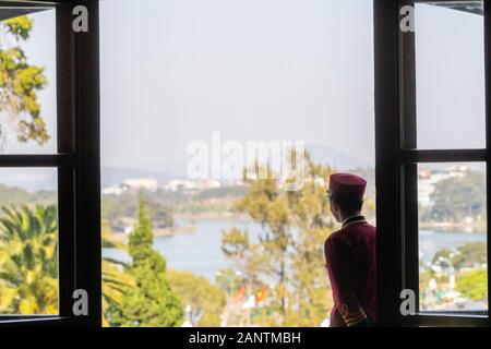 hotel bellboy in french colonial uniform looking out to view of alpine lake and garden with selective focus and blue sky Stock Photo