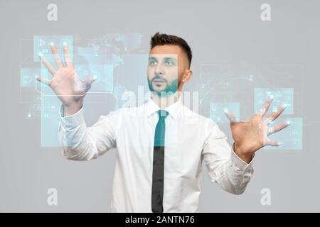 Portrait of young businessman in shirt in office. Selective focus of digital tactile charts screen, bearded man touching virtual icons on projection. Concept of high technologies, digitalization. Stock Photo