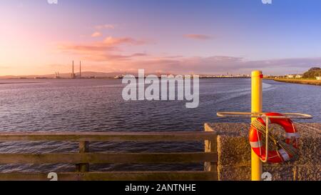 View on Dublin port with Poolbeg Power Plant, tall chimneys and dock cranes from Bull Island. Lifebuoy in first plane. Amazing sunrise, Ireland Stock Photo