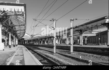 York Railway station where two19th Century canopies of iron and glass cover the platforms.  The platform curves into the station. Black and white. Stock Photo