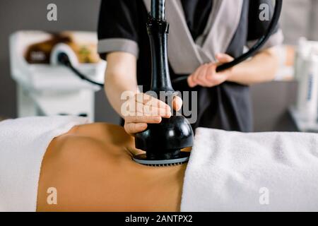 Lymphatic drainage massage device, anti cellulite body correction. Cropped image of woman client receiving vacuum massage of the abdomen and hands of Stock Photo