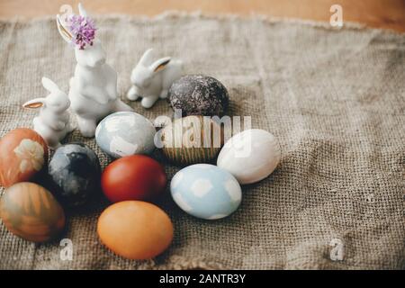 Modern Easter white bunnies and many colorful easter eggs on  rustic fabric. Rural still life. Space for text. Happy Easter. Natural dyed easter eggs. Stock Photo