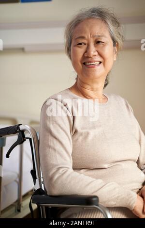 happy senior asian woman sitting in wheel chair in her room in nursing home, happy and smiling