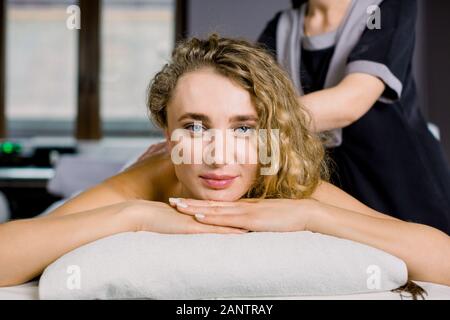 Portrait of young pretty blond woman looking at camera enjoying the procedure of manual back massage. Young woman receiving back massage at spa Stock Photo