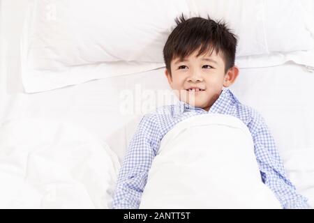 five year old child lying in bed in hospital ward looking happy Stock Photo