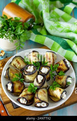 Appetizer stuffed eggplant. Grilled eggplant roll with feta cheese and nuts in a plate on a wooden kitchen table. Stock Photo