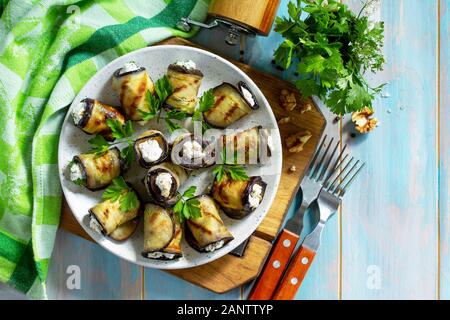 Appetizer stuffed eggplant. Grilled eggplant roll with feta cheese and nuts in a plate on a wooden kitchen table. Top view on a flat background. Copy Stock Photo