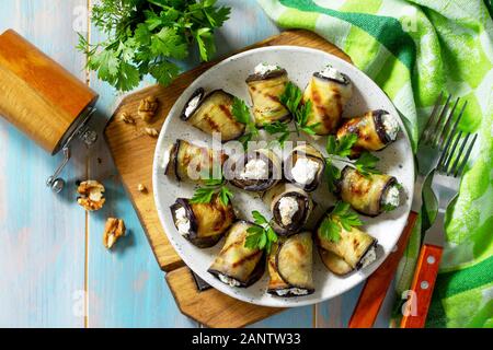 Appetizer stuffed eggplant. Grilled eggplant roll with feta cheese and nuts in a plate on a wooden kitchen table. Top view on a flat background. Stock Photo