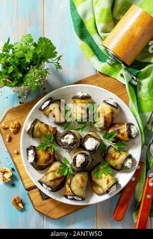 Appetizer stuffed eggplant. Grilled eggplant roll with feta cheese and nuts in a plate on a wooden kitchen table. Top view on a flat background. Stock Photo