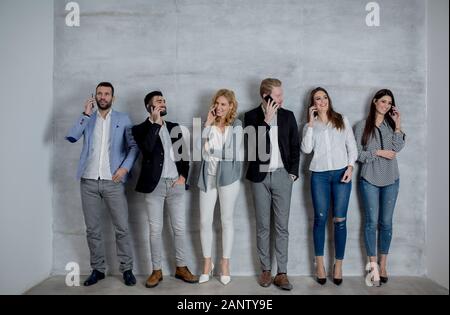 Group of young people with mobile phones standing by the grey wall Stock Photo