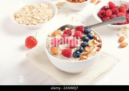 Healthy breakfast. Oatmeal porridge with raspberries, blueberries and nuts in bowl on white table Stock Photo