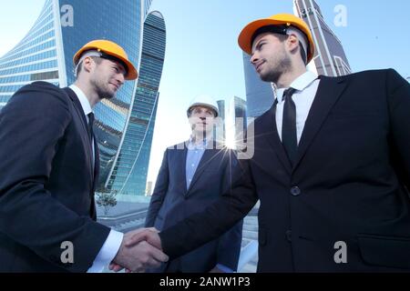 Architect and engineers shaking hands at construction site, skyscrapers on background Stock Photo