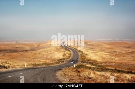 Cars ride on desert road through steppe and hills in Kazakhstan Stock Photo