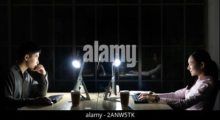 Young adult asian businessman and woman working late at night in their office with desktop computer and laptop. Using as hard working and working late Stock Photo