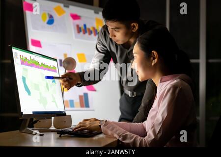 Young adult asian businessman dicuss with collegue about work with analysis graph on white board late at night in their office with desktop computer. Stock Photo