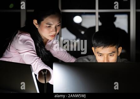 Young adult asian businessman dicuss with collegue about work late at night in their office with desktop computer. Using as hard working and working l Stock Photo