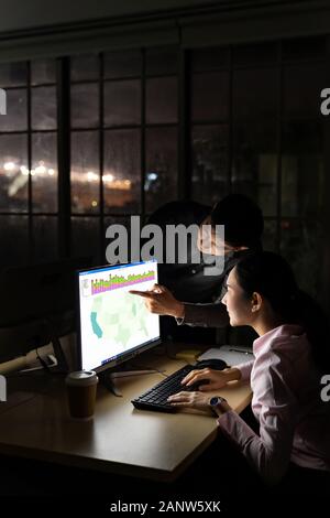 Young adult asian businessman dicuss with collegue about work late at night in their office with desktop computer. Using as hard working and working l Stock Photo