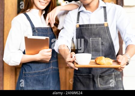 Closeup Asian young adult owners of Small business cafe holding coffee set and digital tablet in front of coffee retail shop. Using as startup SME and Stock Photo
