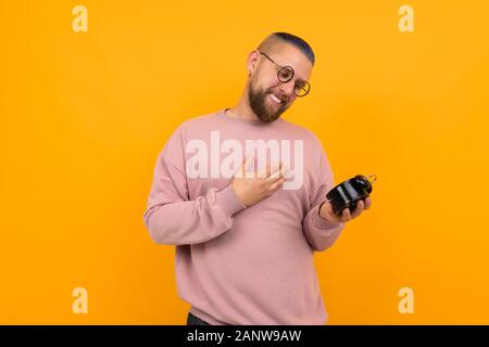 Young strong man with short black hair and glasses holds alarm clock and smiles Stock Photo