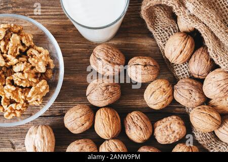 whole walnuts in a cotton bag, scattered nuts on a wooden table. Walnut kernels in a bowl. Stock Photo