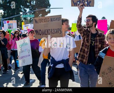 Two men hold up signs at OC Women’s March: “Workers’ Rights Equal Women’s Rights.” A woman wearing a pussyhat holds up a sign asking for equal rights. Stock Photo