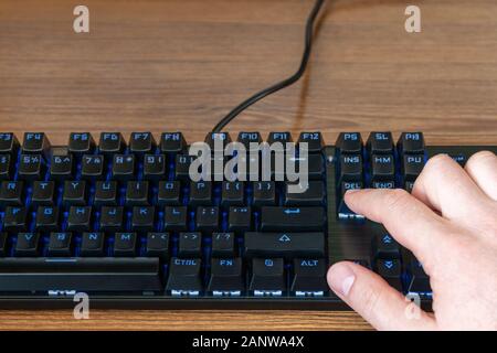 index finger of a male hand presses the delete key on a black keyboard with blue backlight Stock Photo