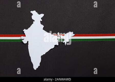 Head-on shot of Indian Map of white color with tricolor ribbon, saffron, green and white color, Indian flag ribbon , on a black background, Paper cut- Stock Photo