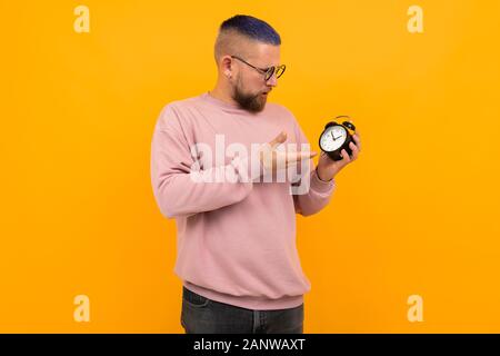 Young strong man with short black hair and glasses holds alarm clock and smiles Stock Photo