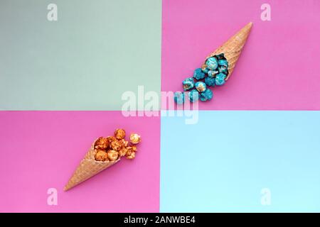 Popcorn spill out from waffle ice cream cone on pastel colorful background. Blue and caramel Popcorn on a cone cornucopia Top view bright hipster Stock Photo