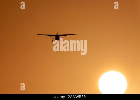 Light aircraft plane landing at London Southend Airport, Essex, UK. Late afternoon in winter. Sunset. Dusk. Cessna airplane over sun disc orange sky Stock Photo