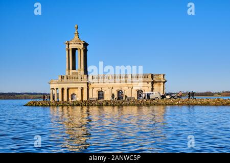Normanton Church situated on the Banks of Rutland Water with a cloudless vibrant blue sky behind and classic cars parked alongside Stock Photo