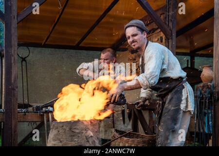 Blacksmiths at work. In the foreground is a master next to an open fire. Forge in the open air during the living history festival Stock Photo