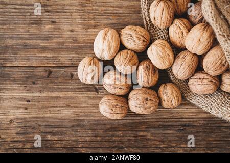 whole walnuts in a cotton bag, scattered nuts on a wooden table. Stock Photo