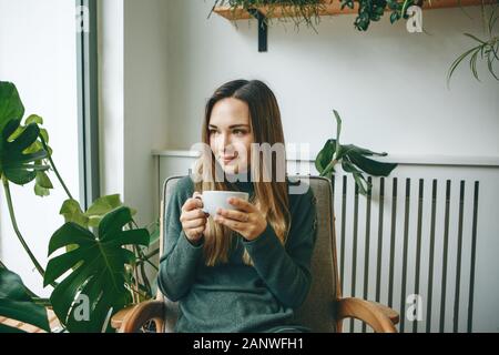 A girl sits in a cafe and drinks a hot drink. She is waiting for someone and she has a meeting or enjoys her morning drink. Stock Photo
