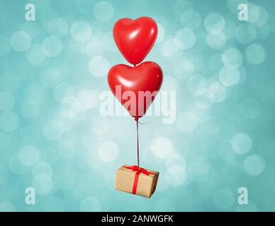 Two heart shaped red air baloon carrying a gift box front of a shiny background. Valentined day and romance concept Stock Photo