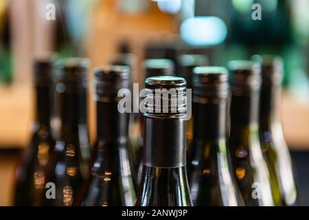dark amber glass wine bottles neck top close up selective focus view, new bottle black seal screw cap on a winery tasting room display, bottling line Stock Photo