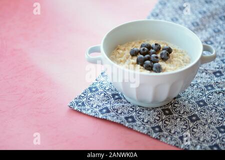 Oatmeal porridge bowl with blueberries for healthy breakfast. Blue napkin and pink background. Delicious organic food. Tasty nutrition way to start Stock Photo