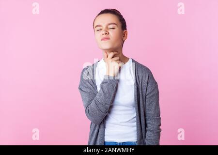 Sore throat. Portrait of sick brunette teenage girl with bun hairstyle in casual clothes touching neck feeling unwell, suffering throat pain, medical Stock Photo