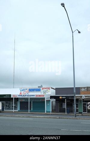 Seafood and Tattoo shops, Carina Heights commercial shopping street. Vertical shot for tall light pole. Stock Photo